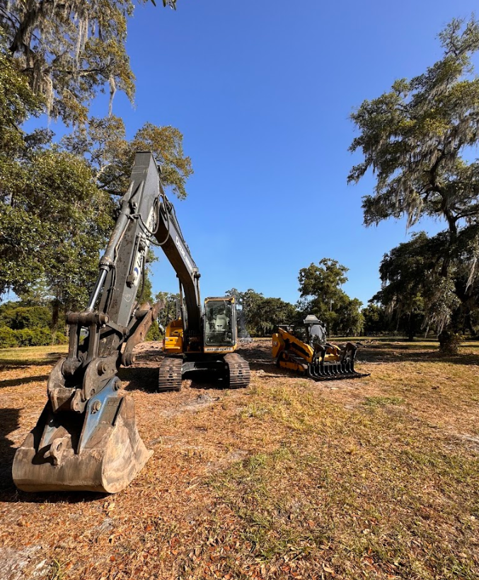 A large excavator is sitting in a field next to a smaller excavator.