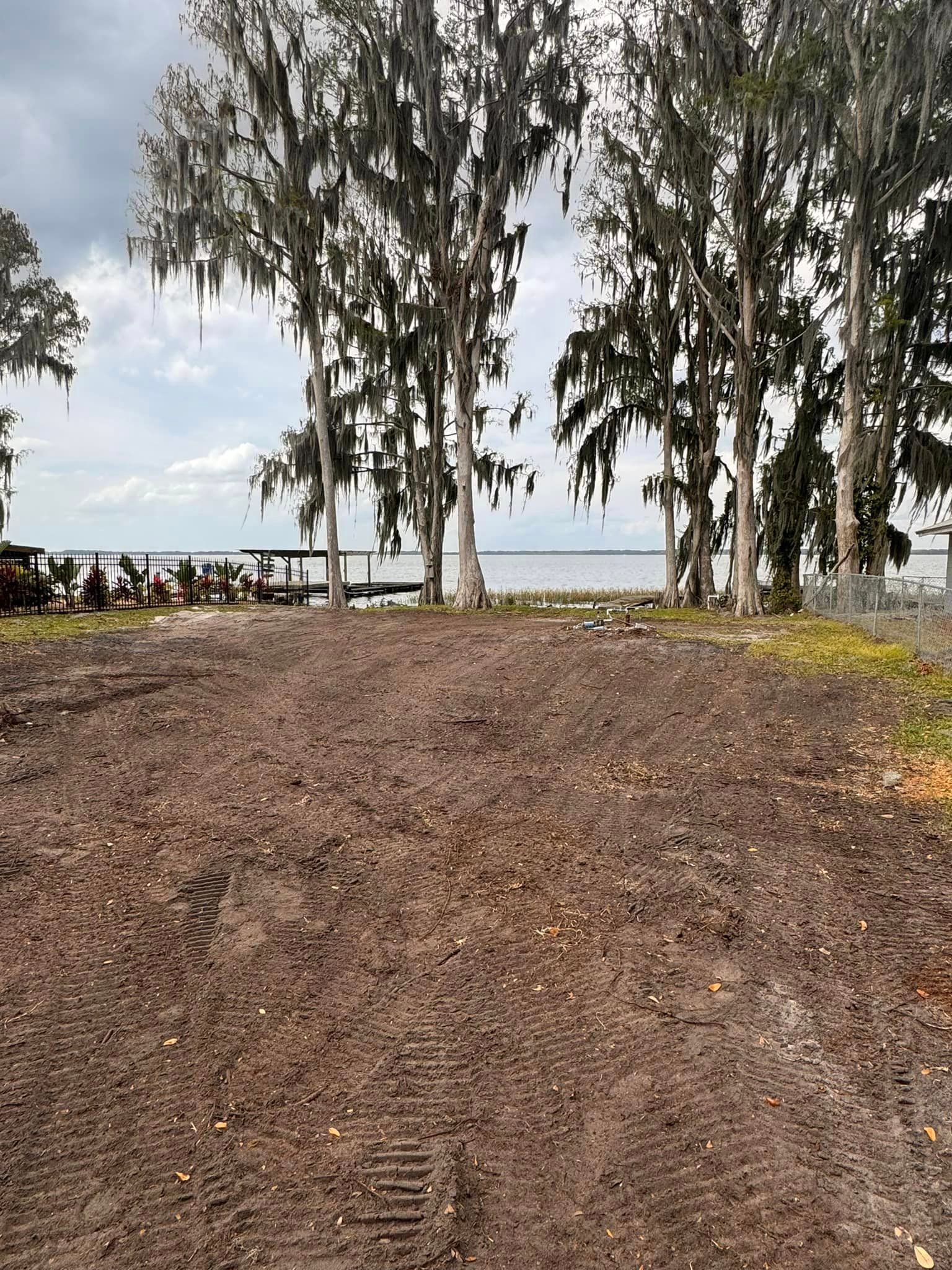 A dirt road with trees in the background and a body of water in the background.
