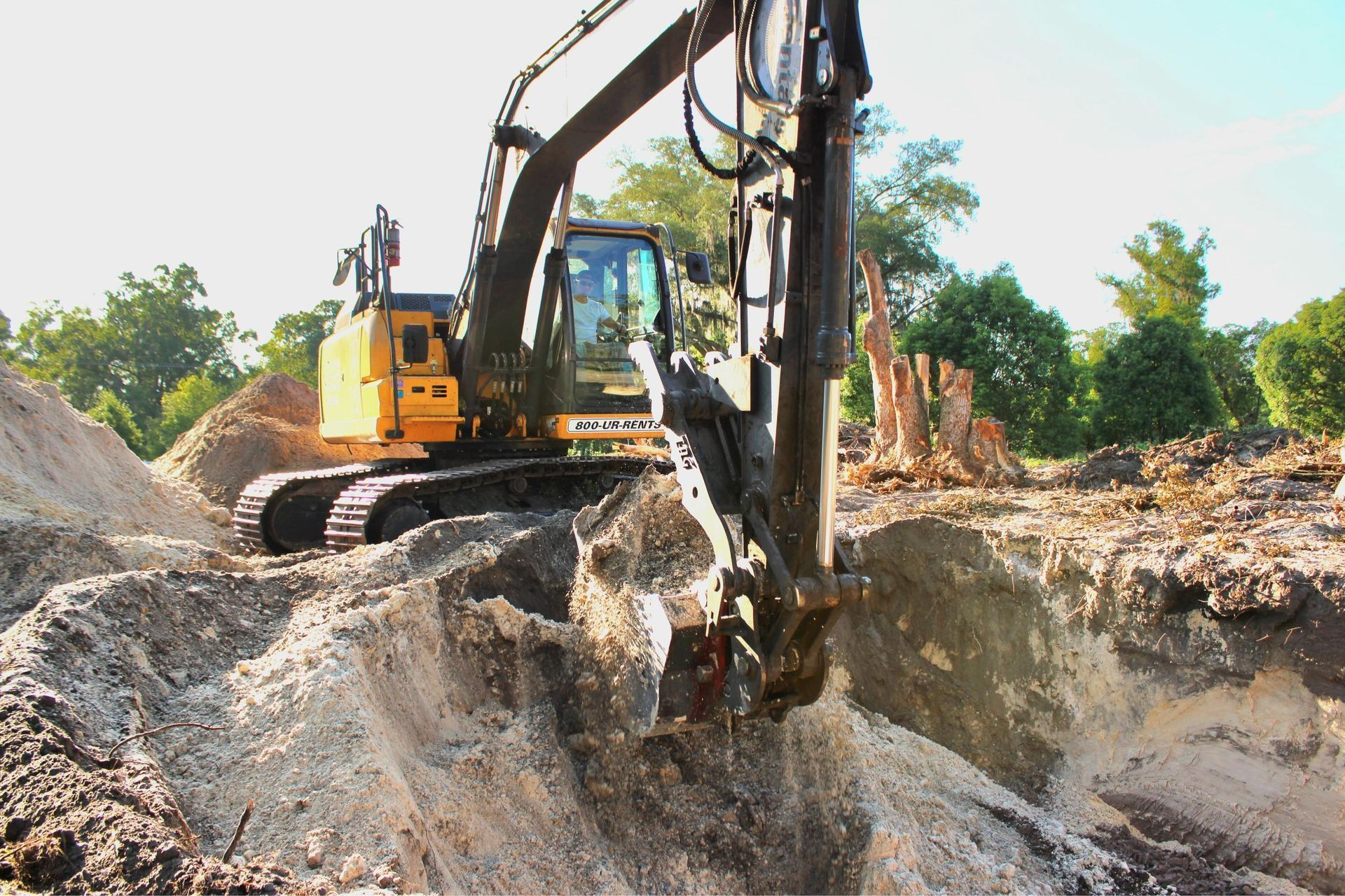 Yellow excavator digging into a mound of dirt on a construction site.