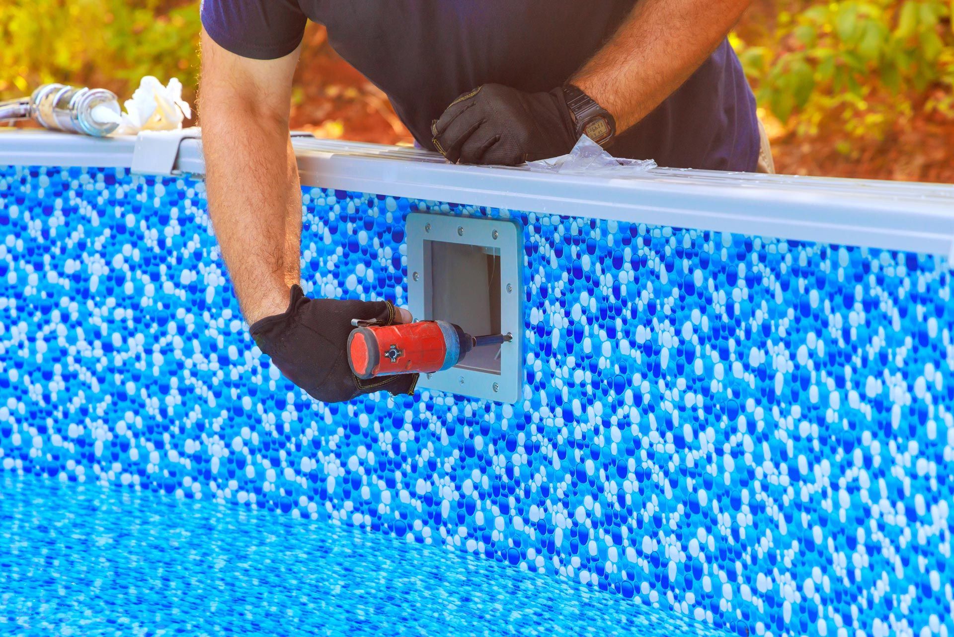 Worker wearing gloves installs a wall fitting inside a blue lined swimming pool.