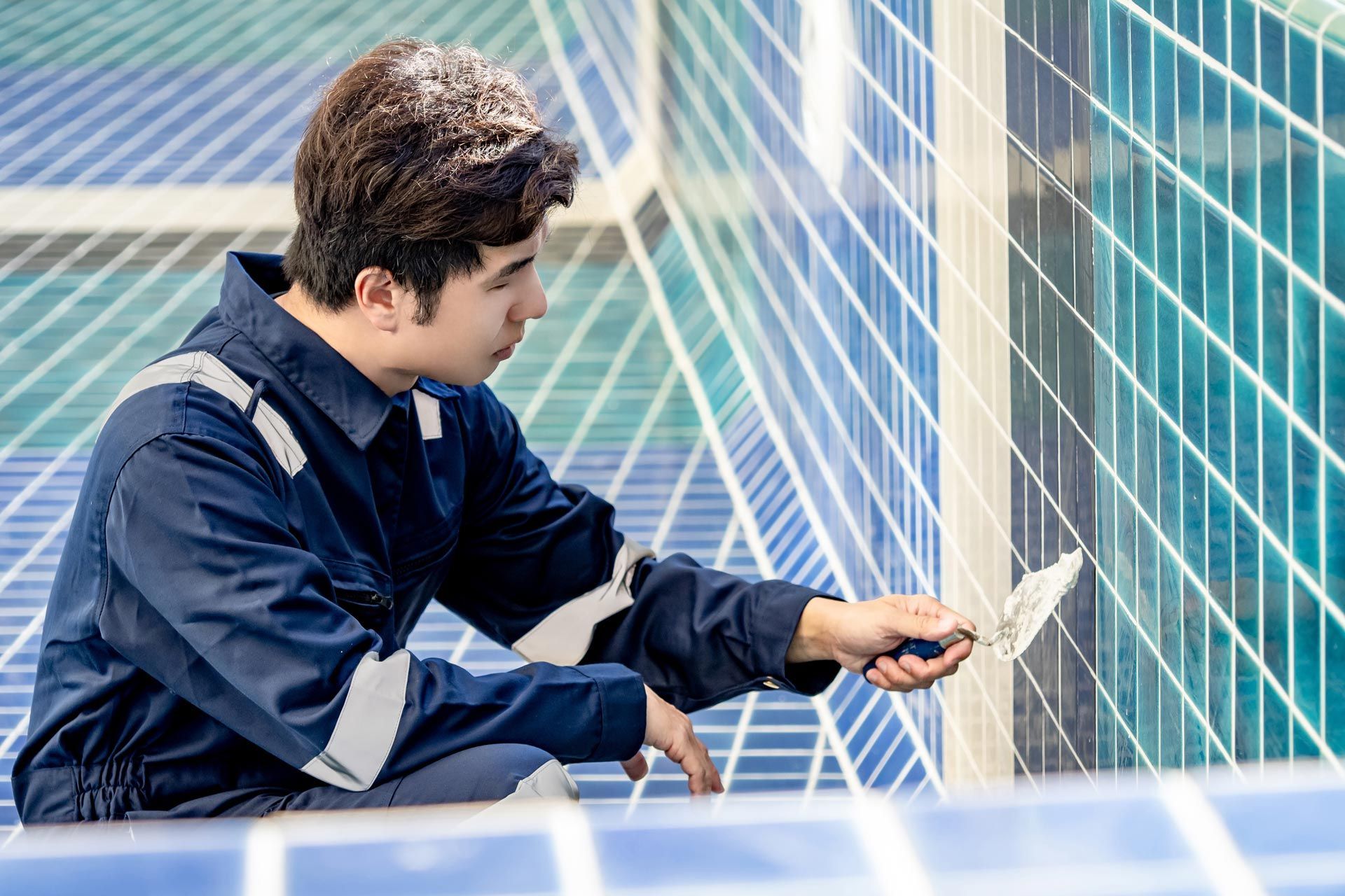 Worker applying grout to blue ceramic tiles during pool remodeling. Worker applying grout to blue ceramic tiles during pool remodeling.