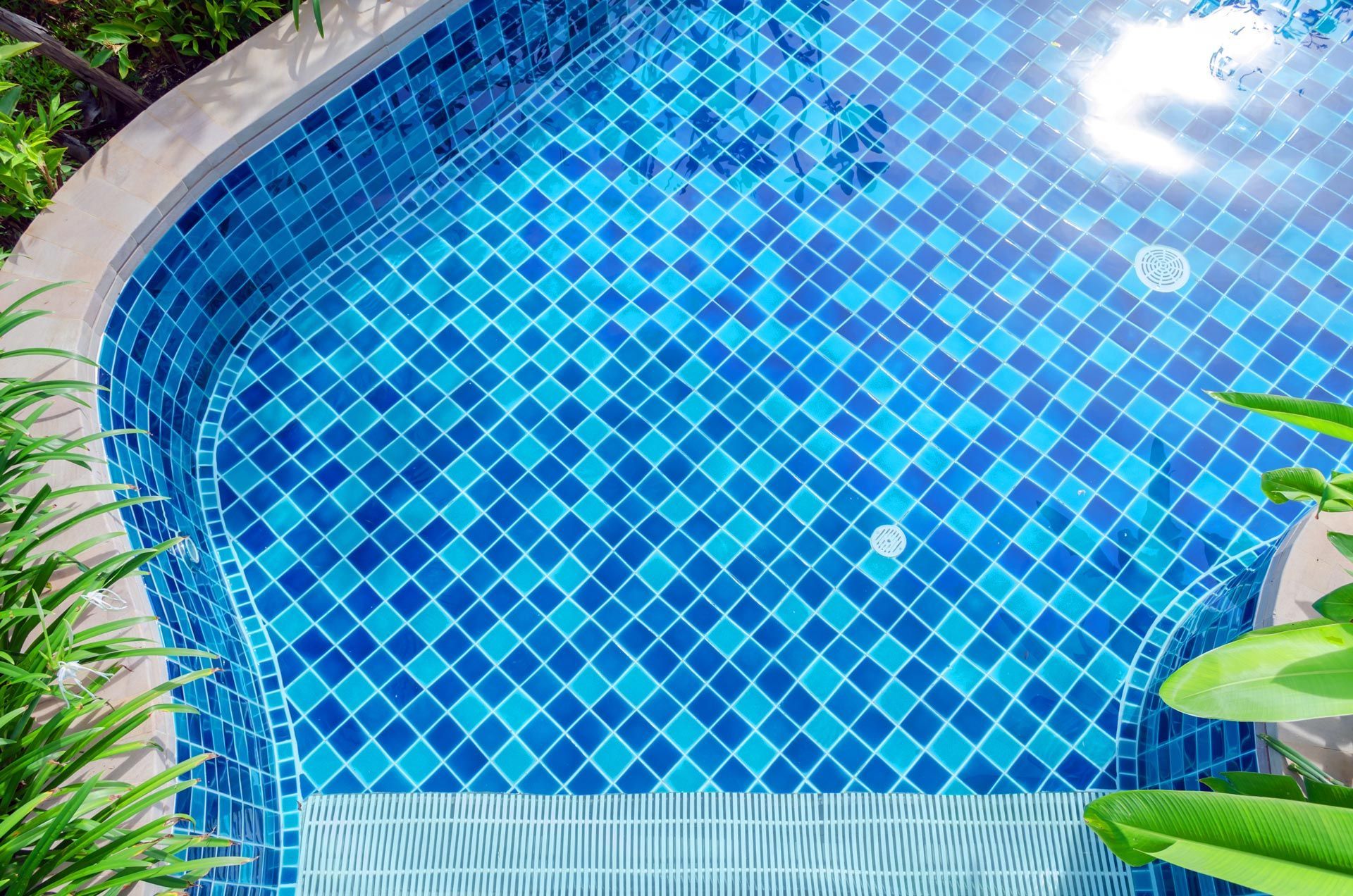 A clear swimming pool with blue mosaic tiles viewed from above, showing clean lines and calm water.