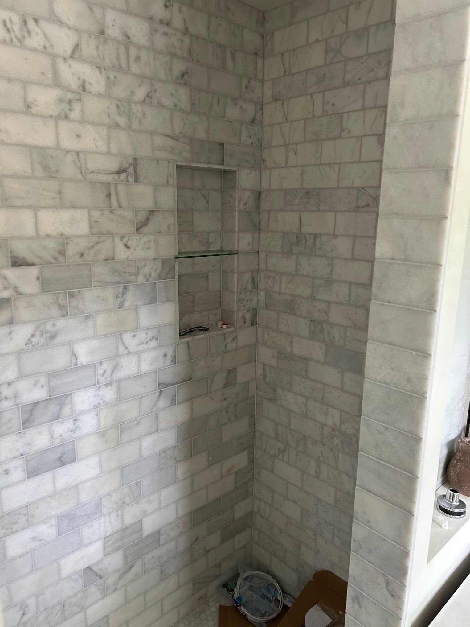 A bathroom with white brick walls and a shower stall.