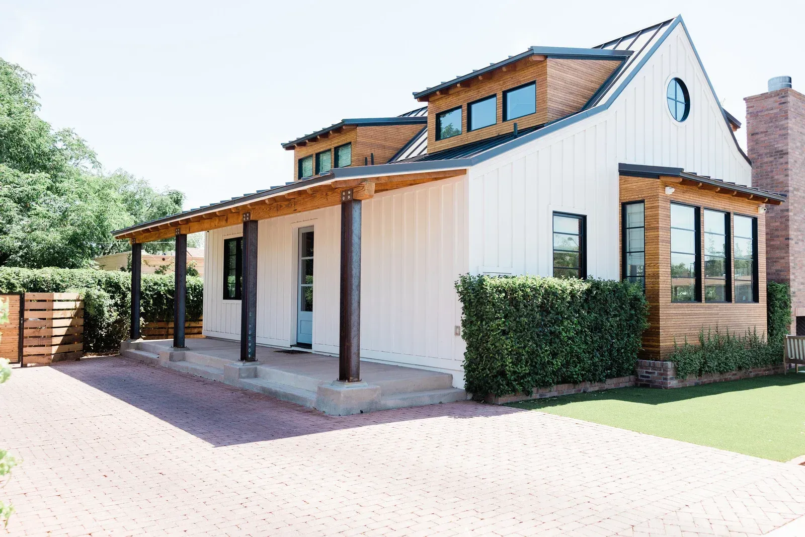 White farmhouse with brown accents, porch, and brick driveway.
