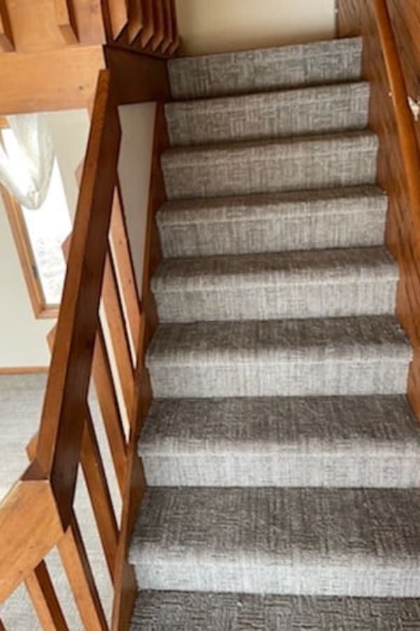 A staircase with light grey patterned carpet and wooden railings viewed from the bottom looking up.