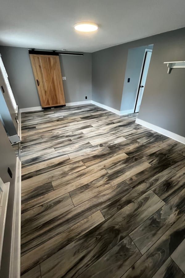 An empty room with wood-look plank flooring, gray walls, a wooden sliding barn door, and a white ceiling light fixture.