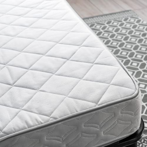A white quilted mattress corner sitting on a black frame next to a gray geometric patterned rug.
