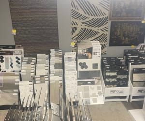 A retail store showroom display featuring a wide variety of tile and flooring material samples organized on shelves.