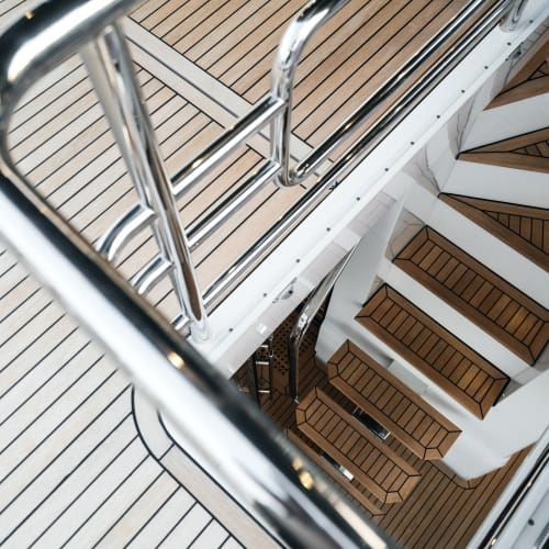 Polished chrome railing overlooking wooden stairs and a teak deck on a luxury boat.