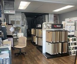 A showroom featuring racks of various wood flooring samples, a beige office chair, and overhead lighting.