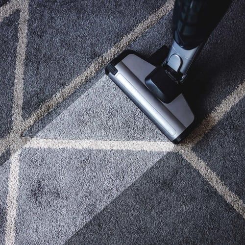 A vacuum head cleaning a grey rug with a white geometric line pattern.