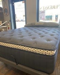 A grey, tufted mattress on an adjustable base in a showroom with a window in the background.