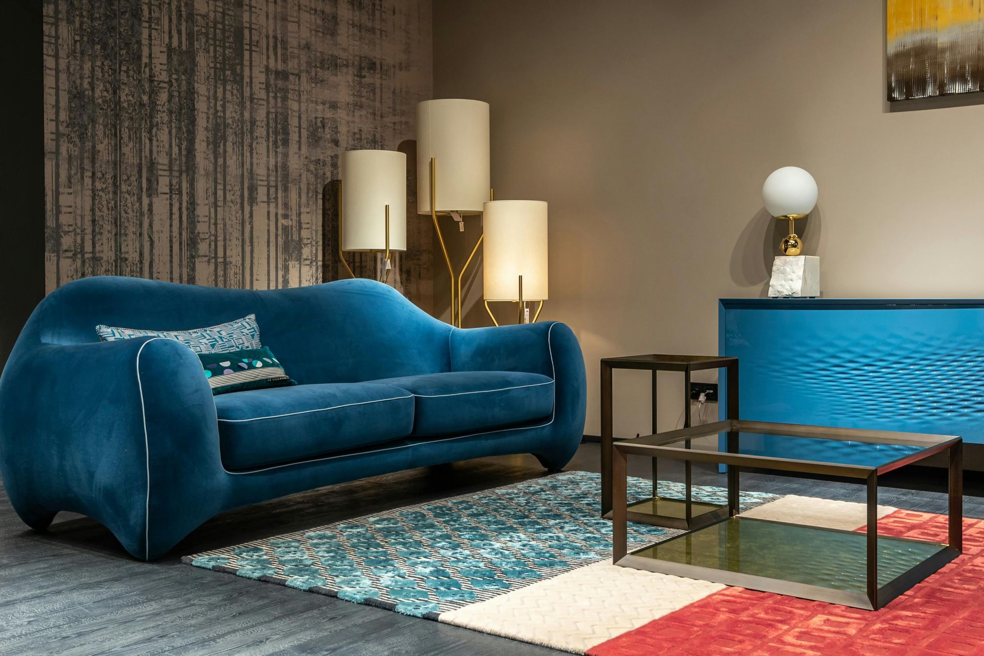 A teal velvet sofa sits on a patterned rug next to a modern coffee table, side table, and floor lamps in a room.