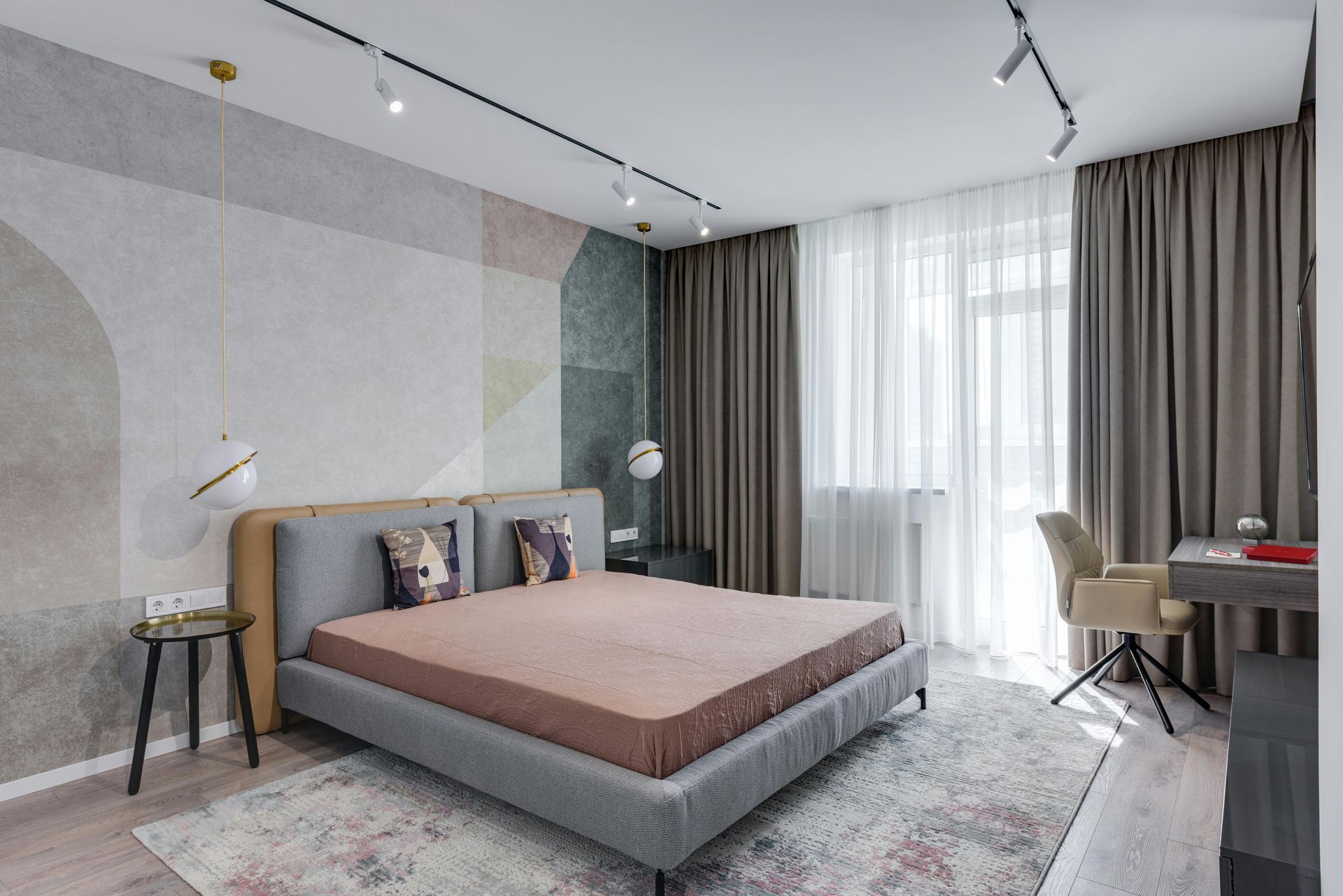 Modern bedroom featuring a gray bed, patterned wallpaper, brown curtains, a desk with a chair, and a decorative rug.