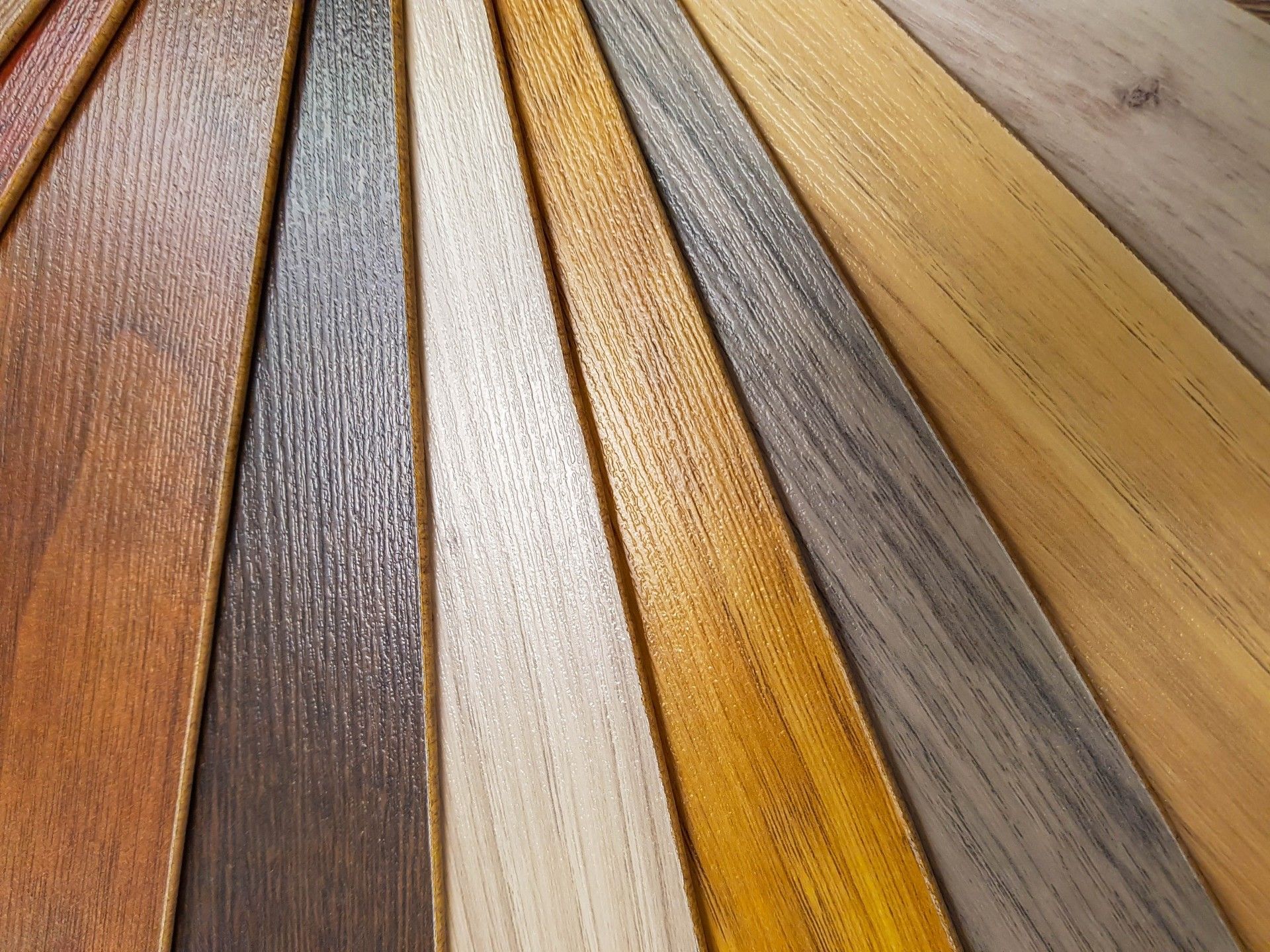 A fan-shaped arrangement of various wood flooring samples in shades ranging from light beige to deep brown and gray.