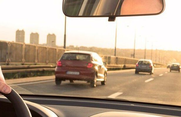 A person is driving a car on a highway and looking at the rear view mirror.