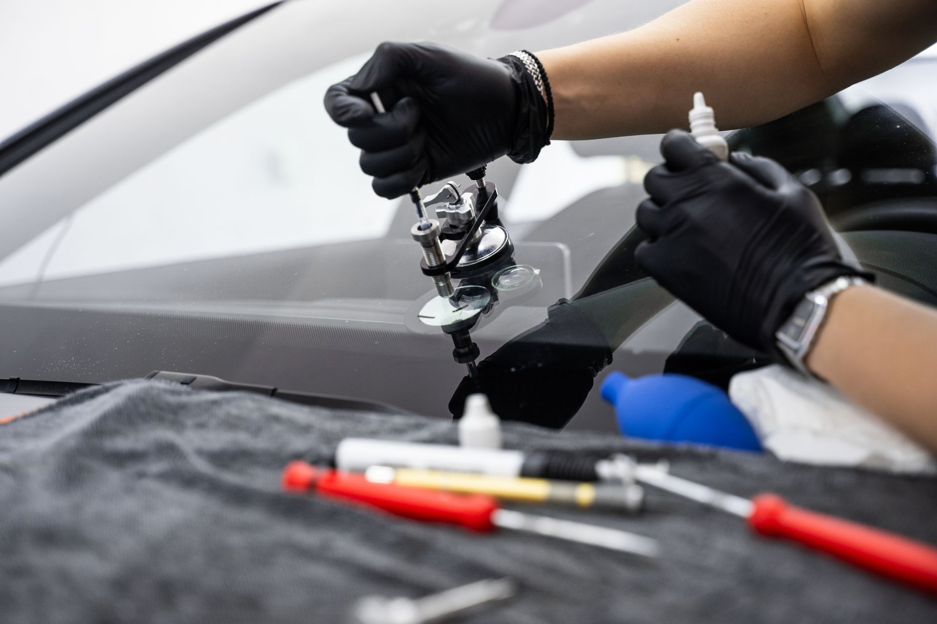 Gloved hands using tools to inject resin into cracked windshield during repair process.