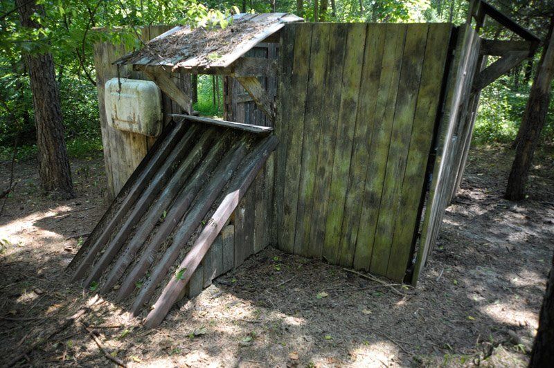 A wooden shed in the middle of a forest with a sink on top of it.