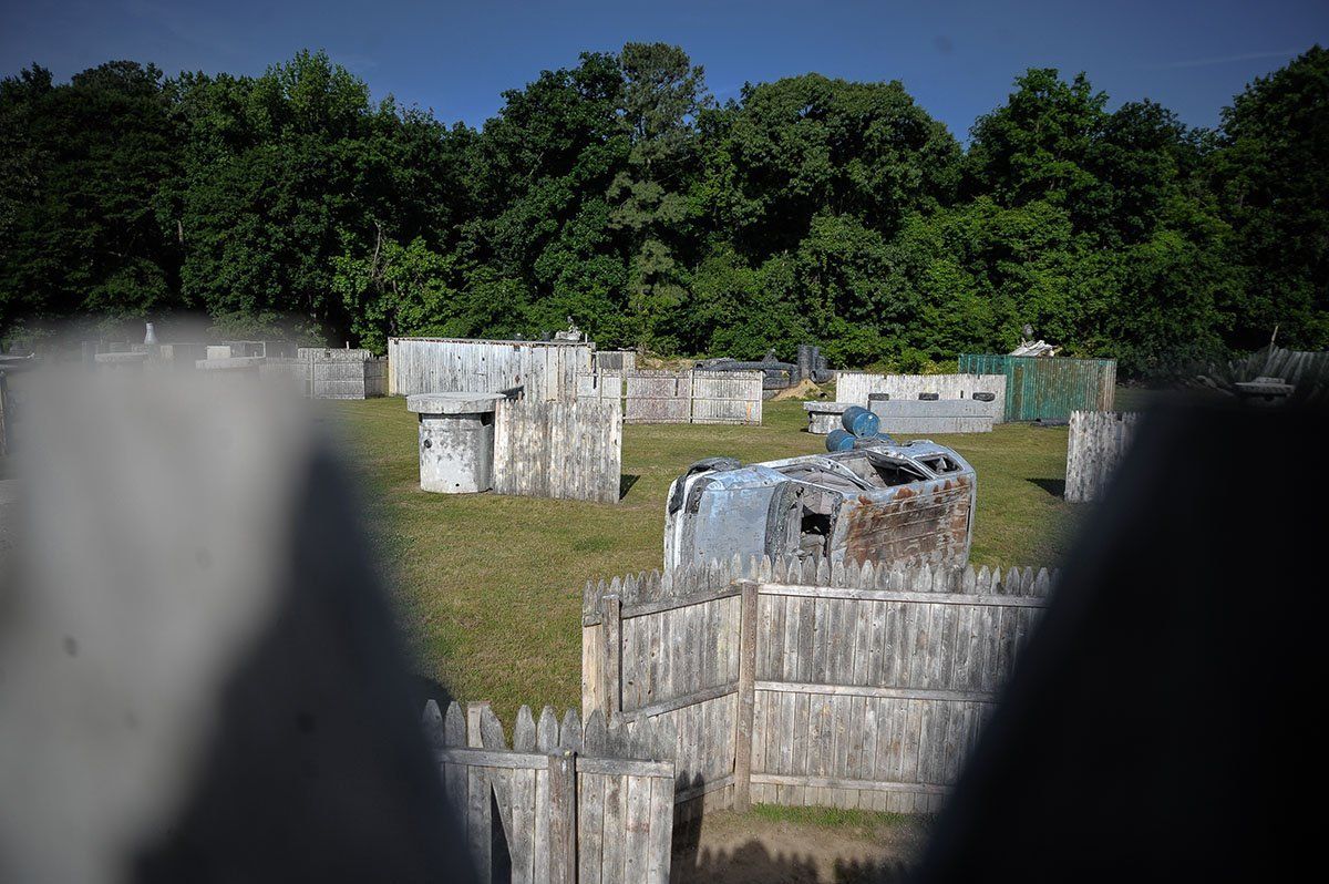 A person is playing paintball in a field with trees in the background.