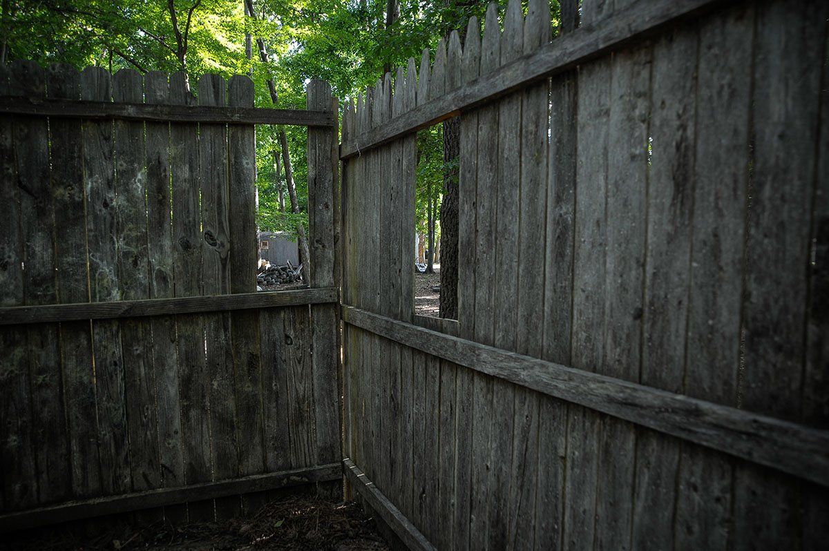 A wooden fence with a hole in it and trees in the background.