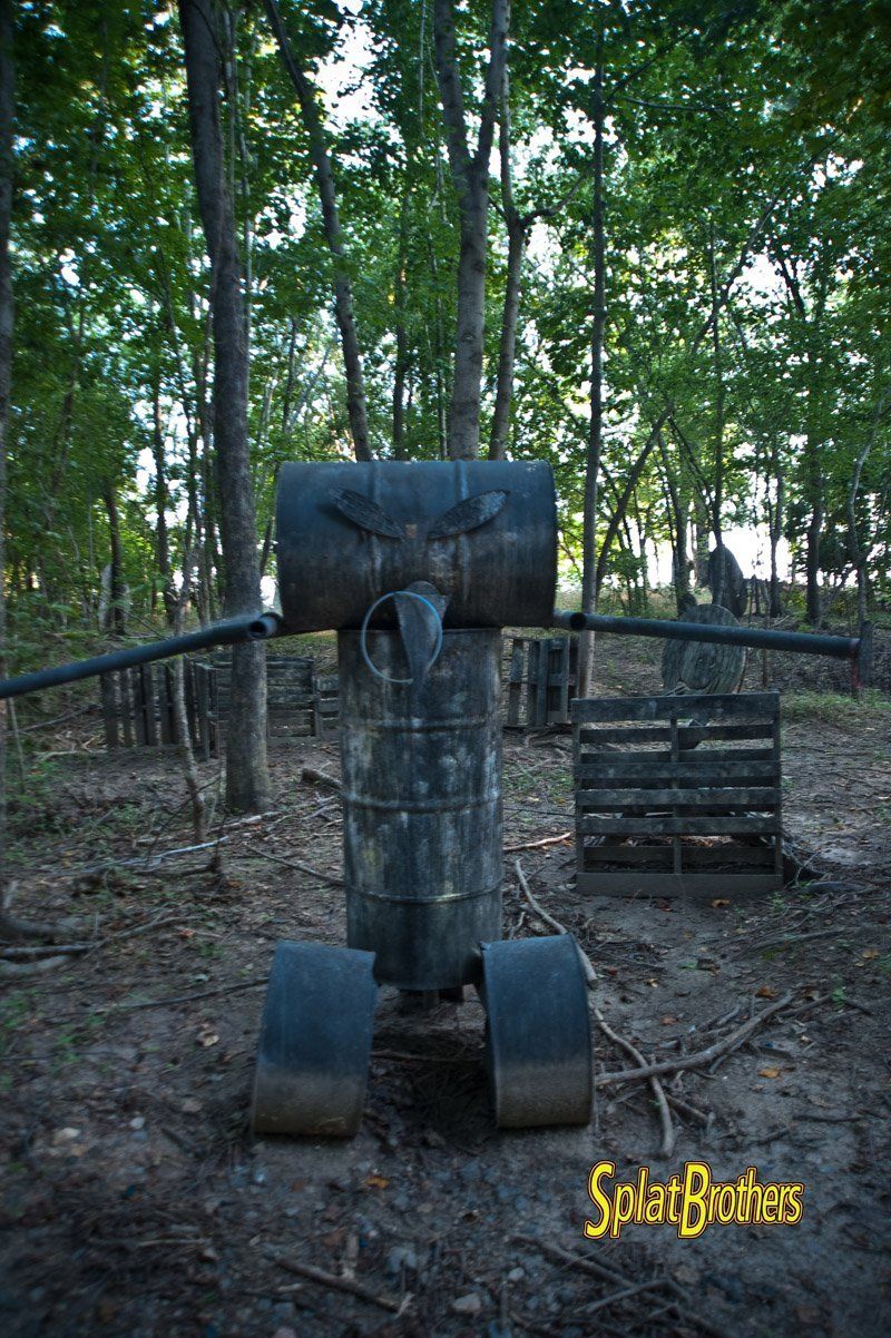A robot made out of barrels is in the middle of a forest