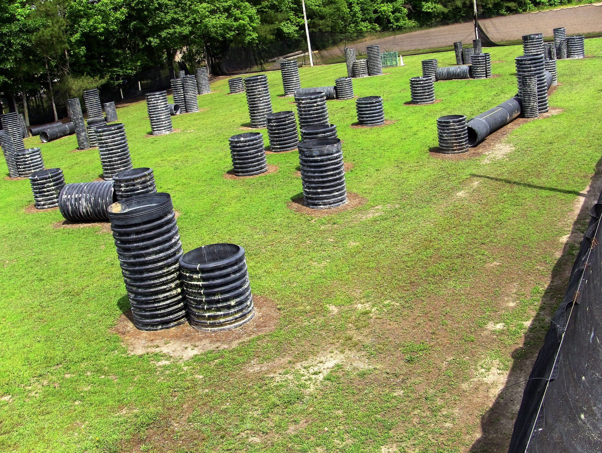 A paintball field with a lot of barrels in the grass.