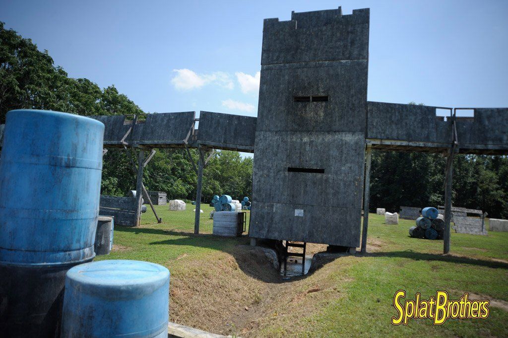 A paintball field with blue barrels and a castle in the background.