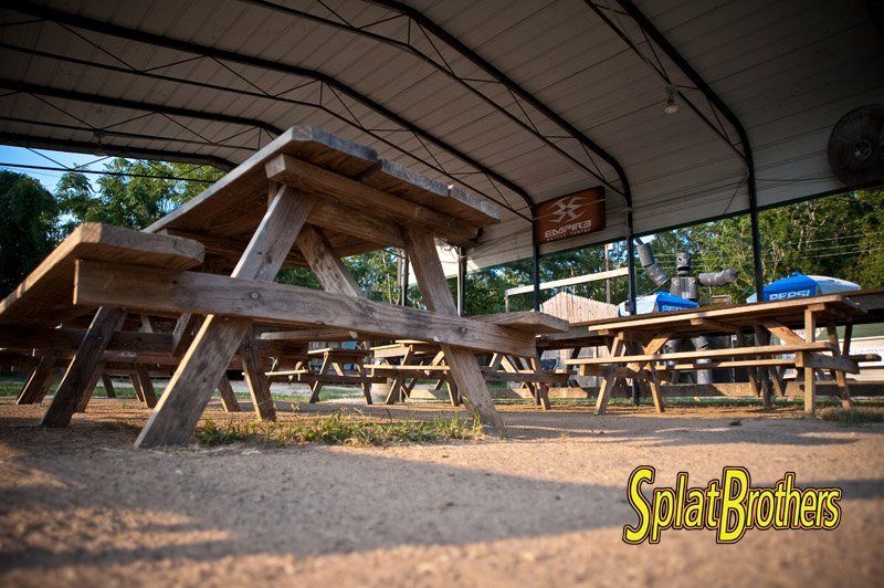 A group of wooden picnic tables under a canopy with the words splat brothers on the bottom