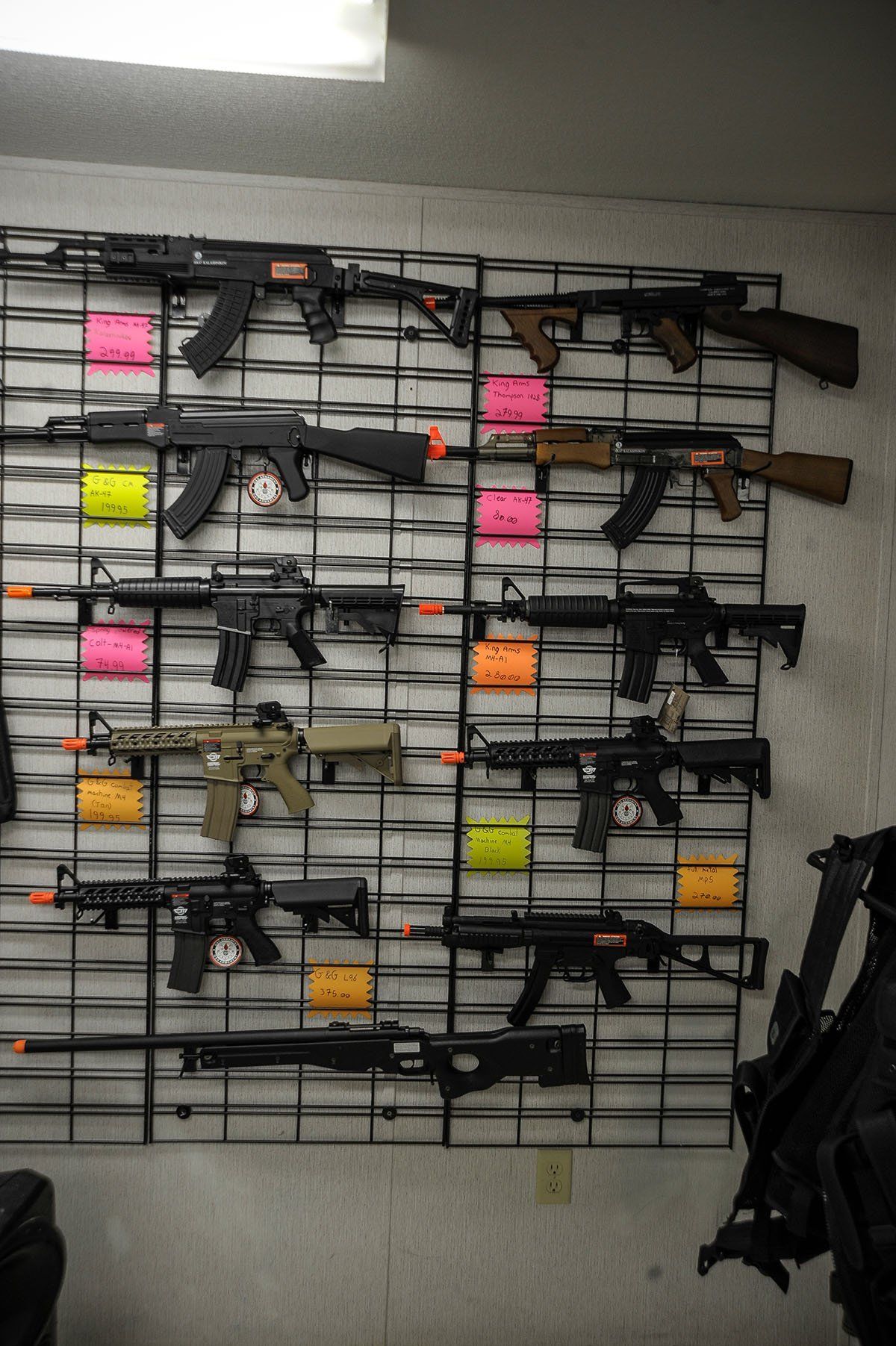Guns displayed on a wall grid. Pink and yellow price tags are visible.
