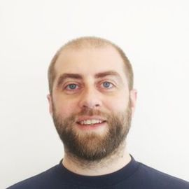 A man with a beard is smiling for the camera while wearing a blue shirt.