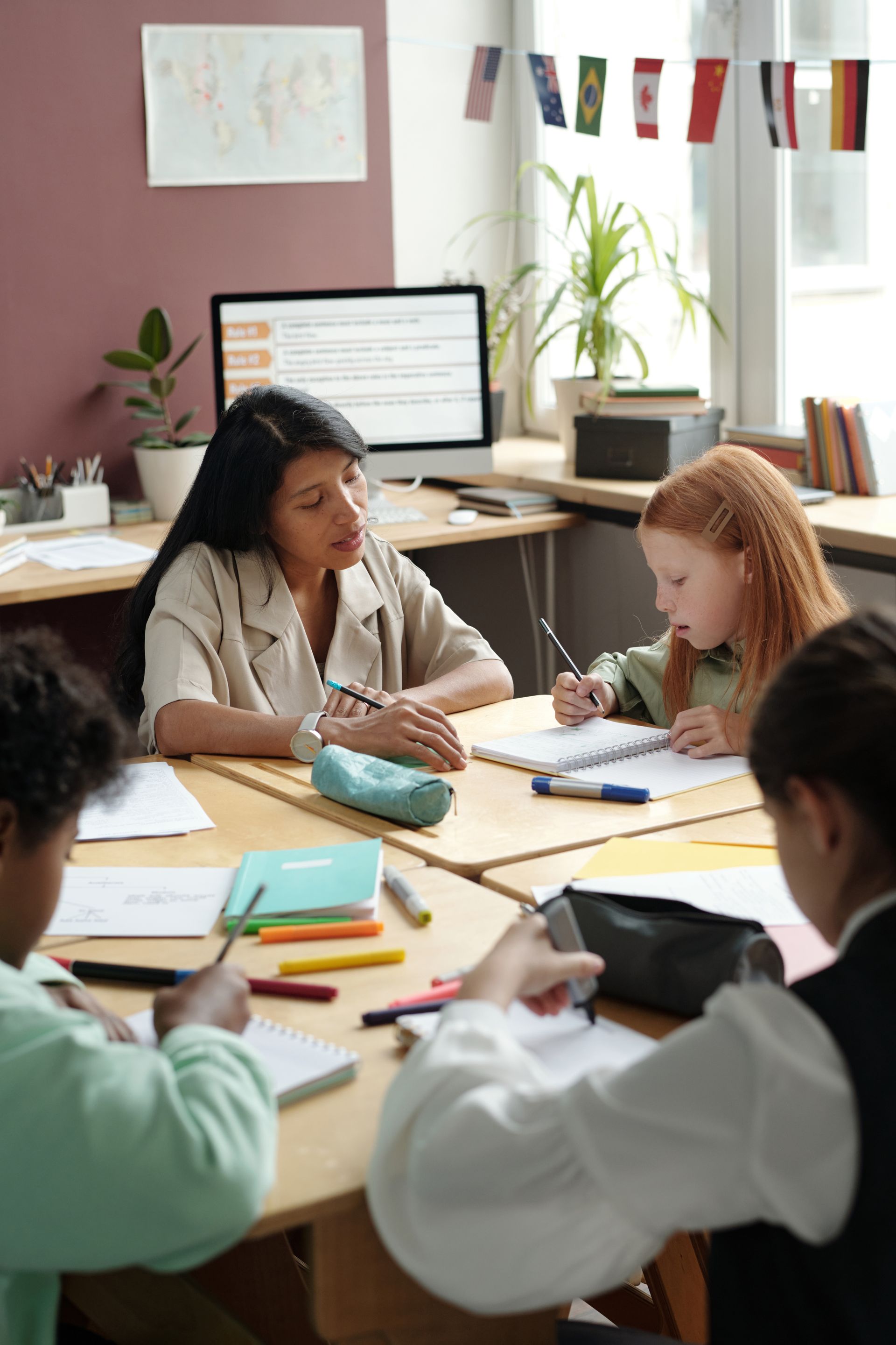 A group of children are sitting at tables in a classroom with their teacher.