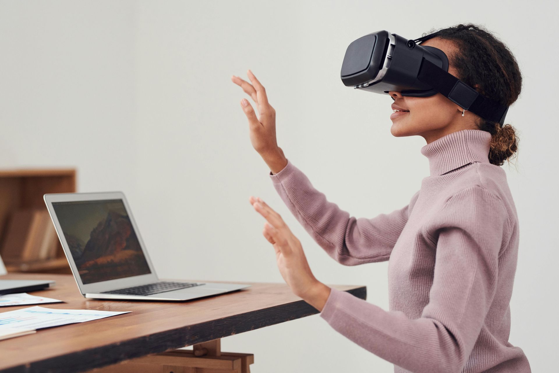 A woman is wearing a virtual reality headset in front of a laptop computer.