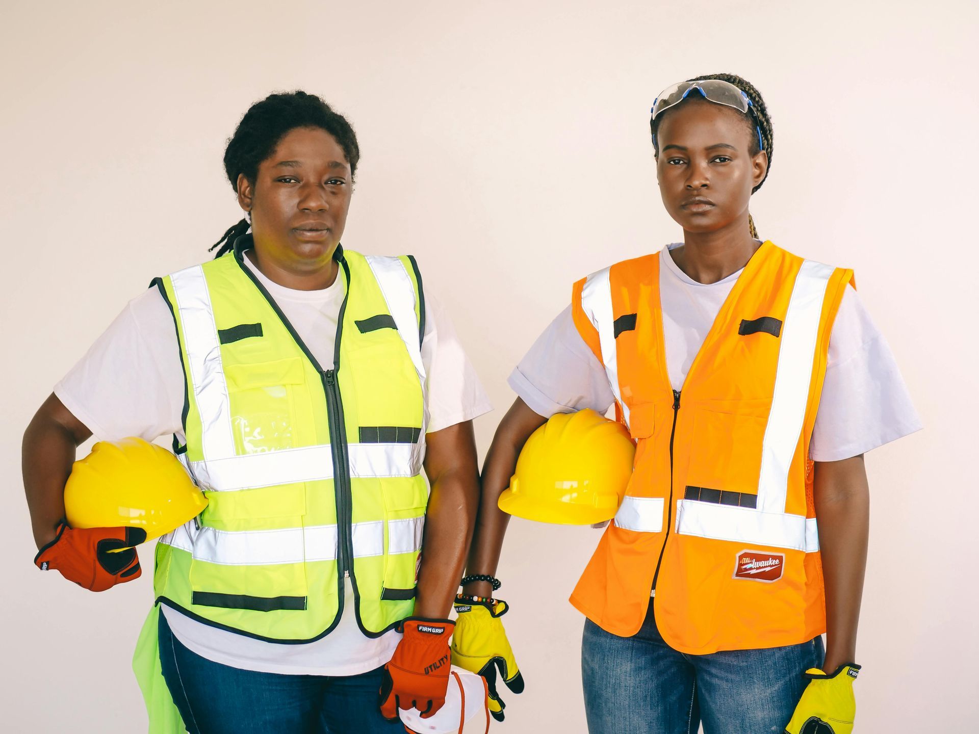 Two women wearing safety vests and hard hats are standing next to each other.