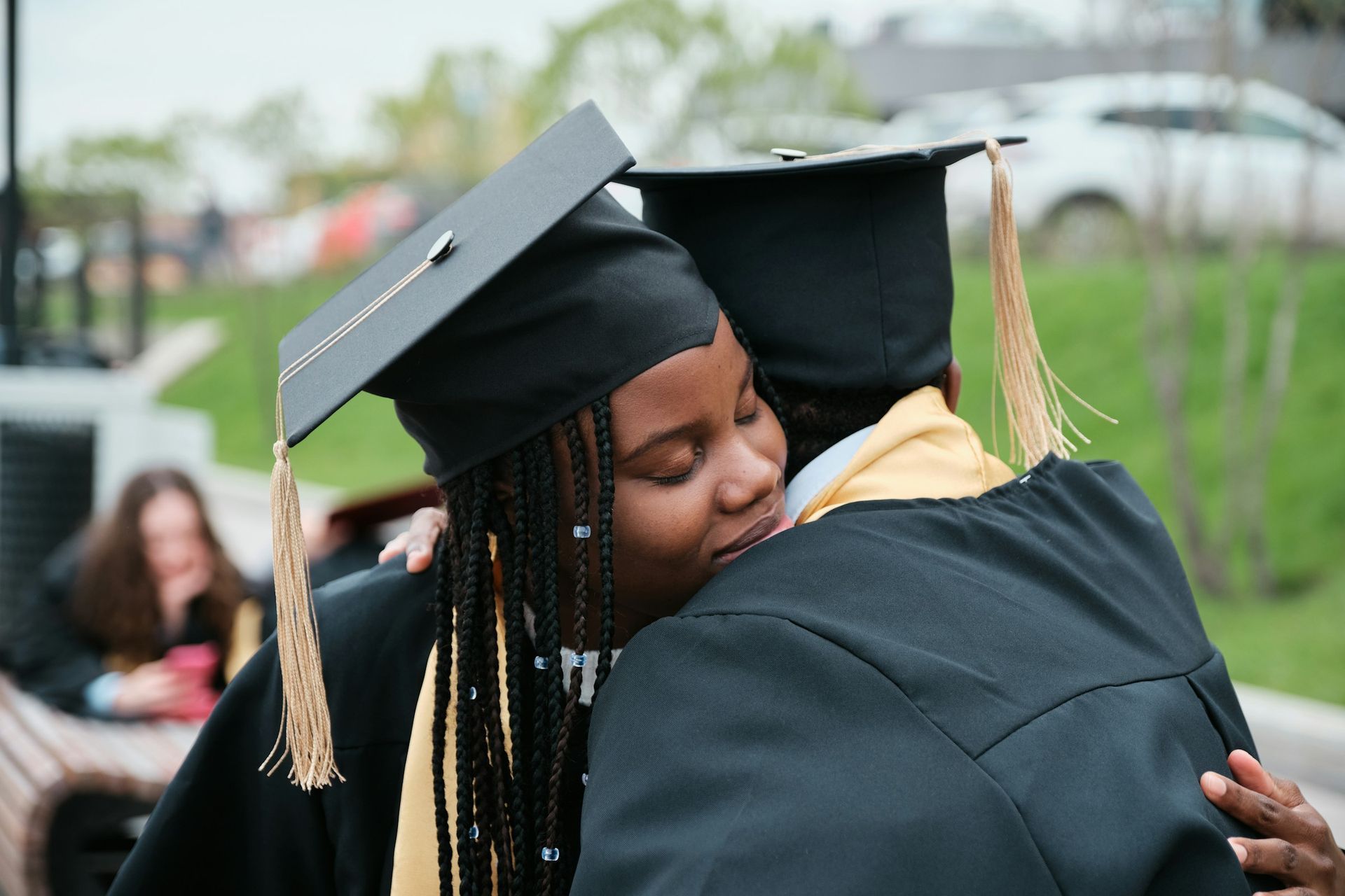Two successful scholarship recipients in black caps and gowns share an emotional hug after their uni