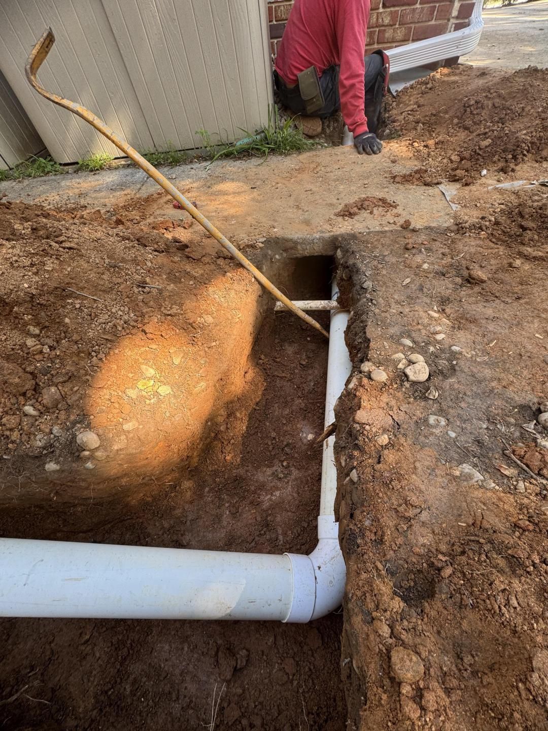 A person installing white PVC drainage pipes in a trench outdoors.