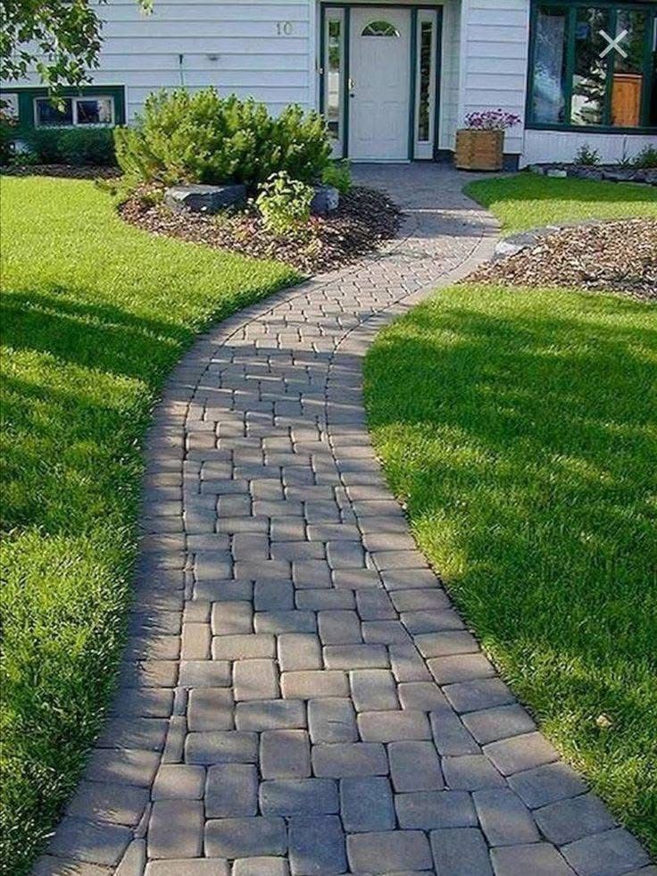 Stone path curves through green lawn to a white house's front door.