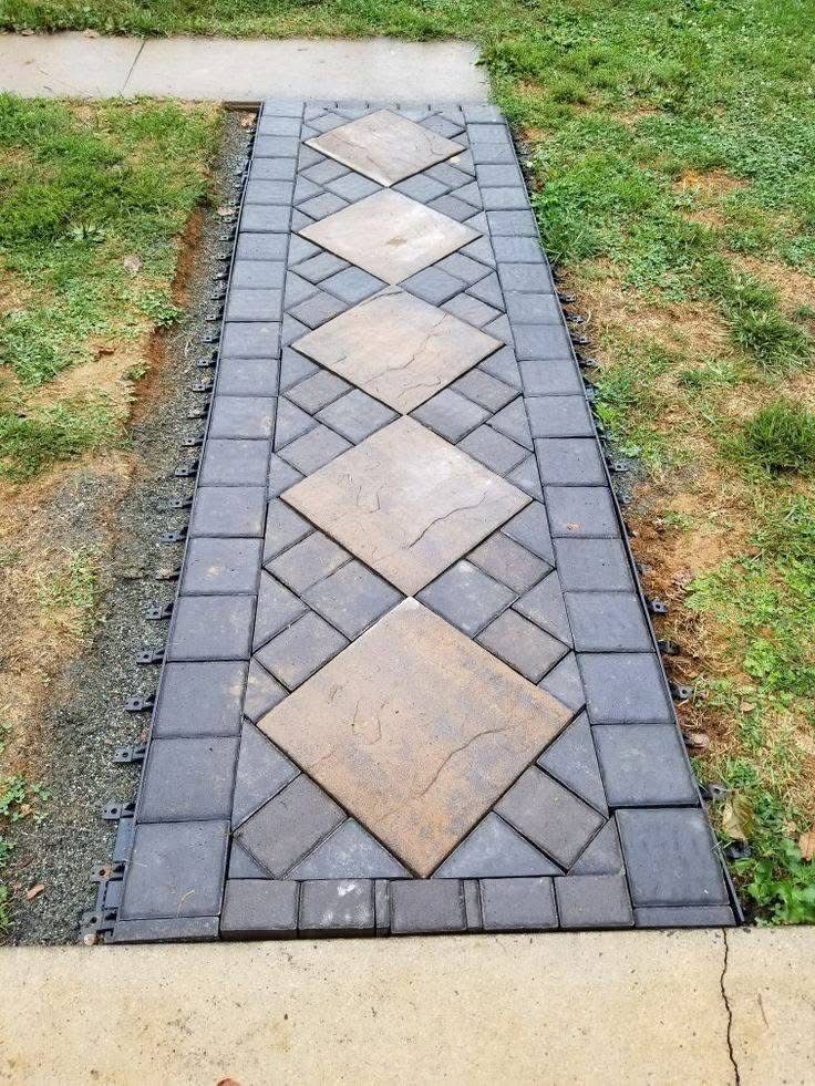 A brick walkway with tan diamonds and dark gray squares, framed by a concrete border, set in grass.
