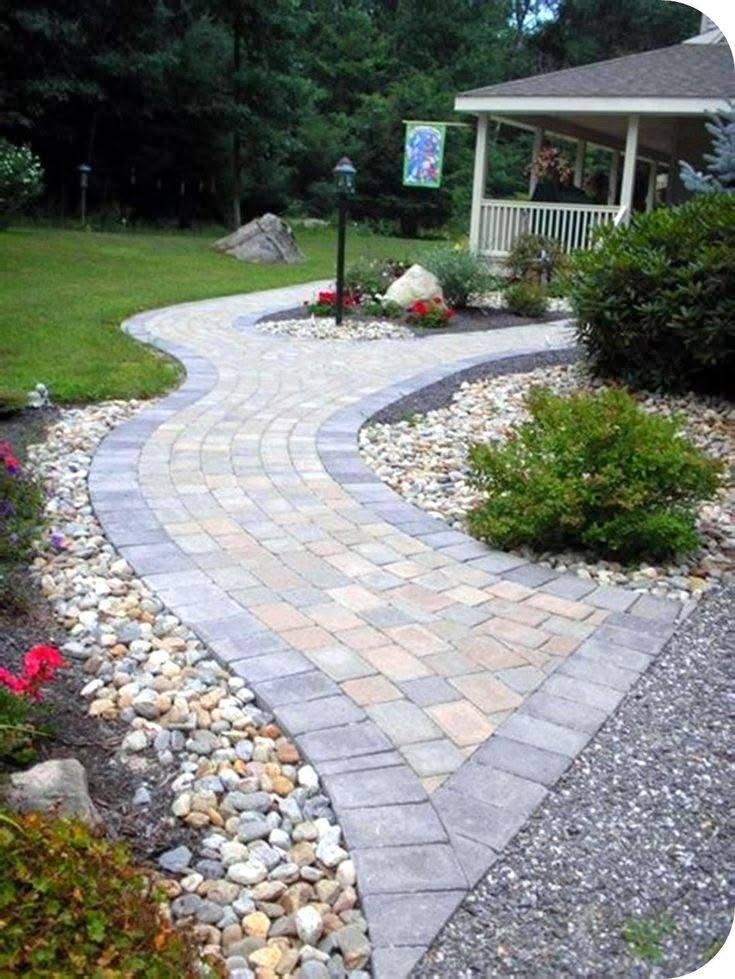 Curving brick pathway with rock and flower borders leading to a house with a porch.