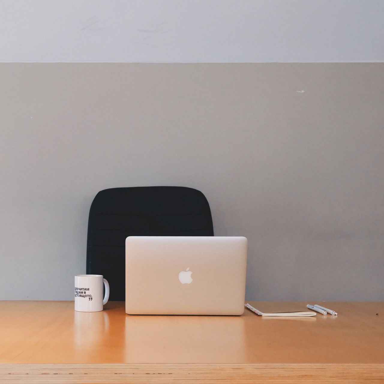 An apple laptop sits on a desk next to a coffee mug