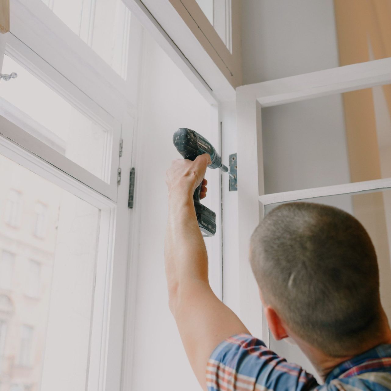 A man is using a drill to fix a window