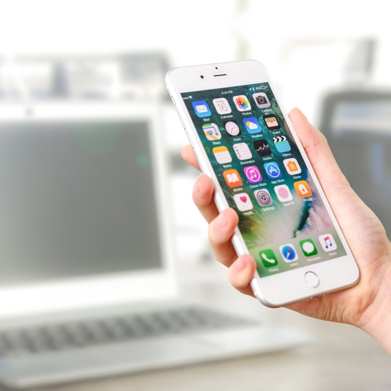 A person is holding a cell phone in front of a laptop.