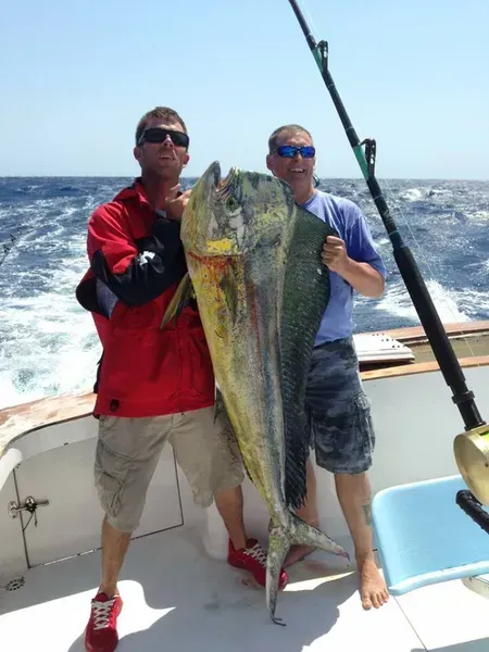 Two men on a boat holding a large, colorful mahi-mahi fish they caught.