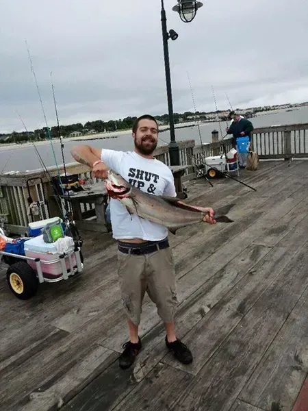 Man on a pier holding a large fish. Wearing a 