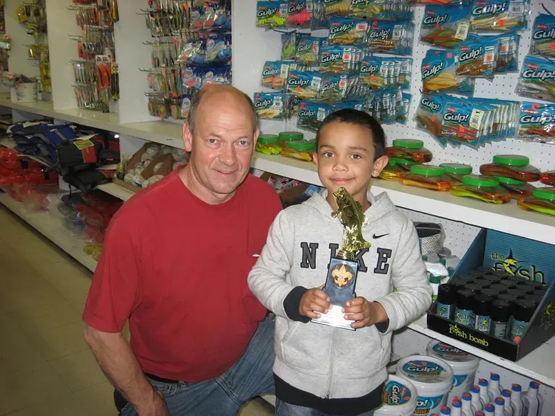 Man and young boy in a store, posing with a trophy. The boy is smiling and holding the trophy.