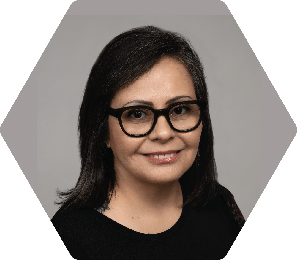 Julissa Ricks with dark hair and glasses smiles at the camera, inside a gray hexagon frame.