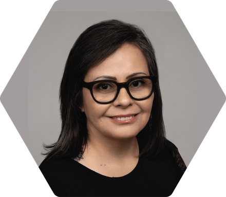 Julissa Ricks with dark hair and glasses smiles at the camera, inside a gray hexagon frame.