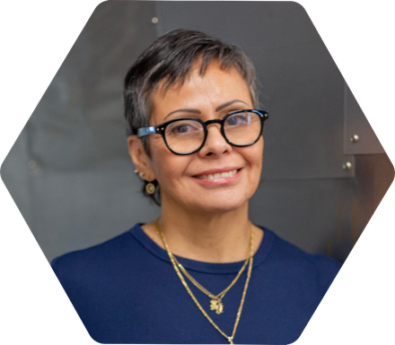 Julissa Ricks with dark hair and glasses smiles at the camera, inside a gray hexagon frame.