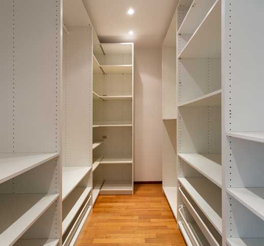 Empty walk-in closet with white shelves and parquet 
