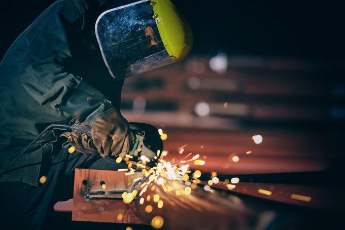 Un saldatore con indumenti protettivi produce scintille su metallo in un'officina buia.