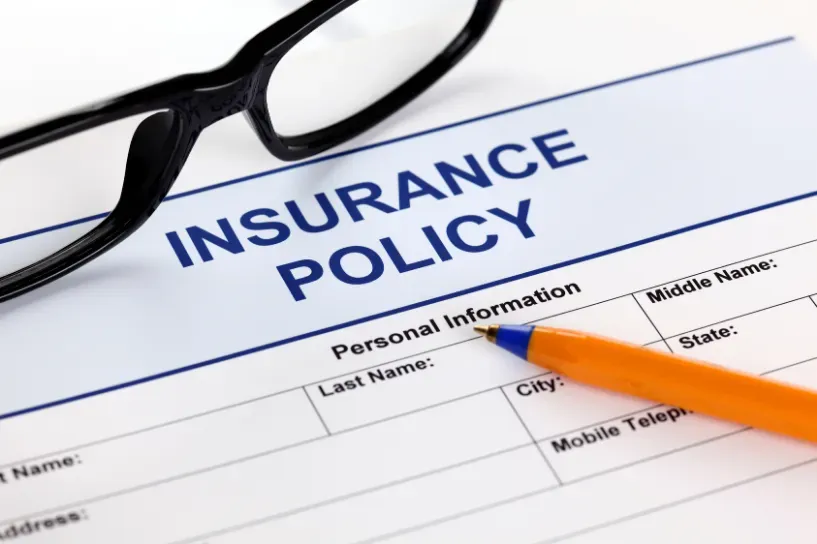 Insurance policy form with eyeglasses and orange pen on a white desk
